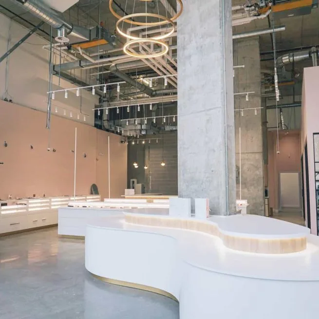 Engage Studio's Bloor Street showroom: a curved white display counter beneath a concrete column and a ring-light chandelier