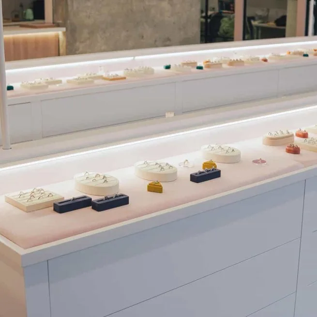 Rings on trays and ring boxes along the lit edge of a display counter at Engage Studio