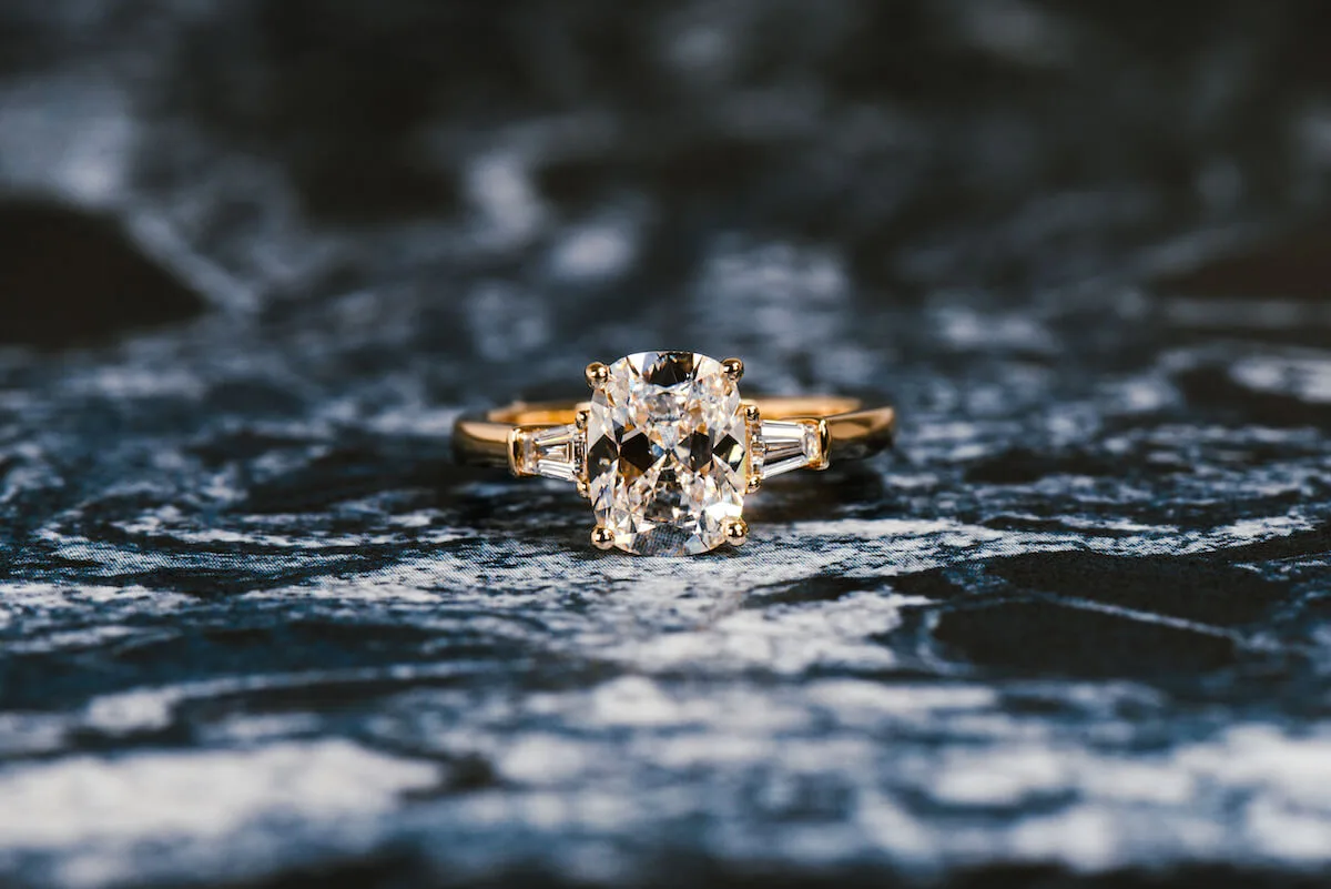 Elongated cushion-cut diamond engagement ring in yellow gold with tapered baguette side stones, on dark blue marble