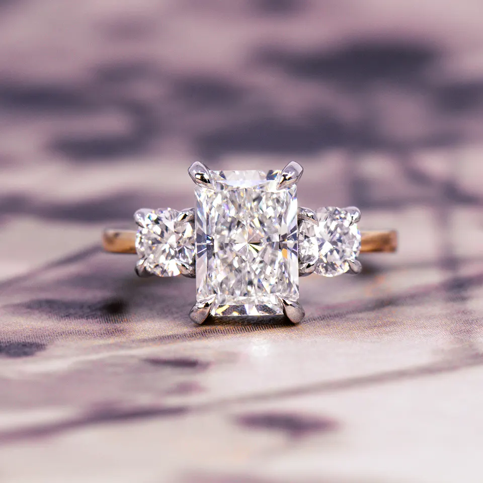 Radiant-cut diamond three-stone engagement ring with two cushion-cut side diamonds in white claws on a yellow gold band