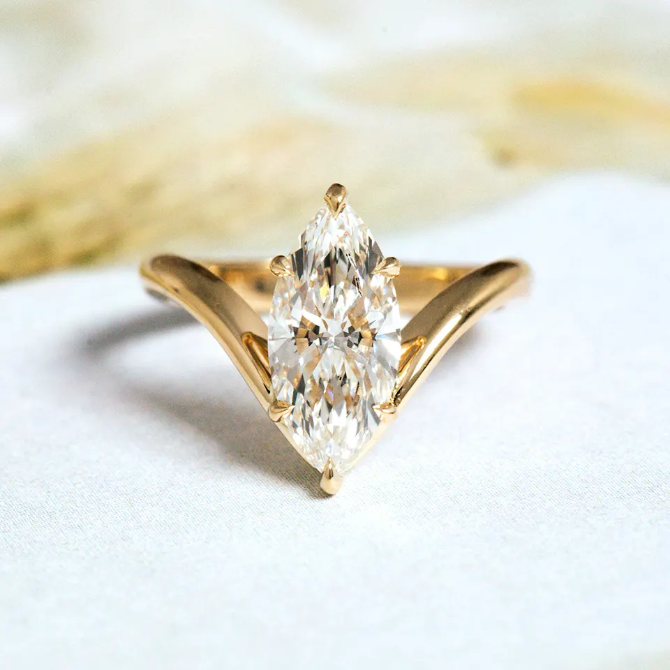 Marquise-cut diamond engagement ring on a V-shaped yellow gold band that follows the stone's point, on white fabric