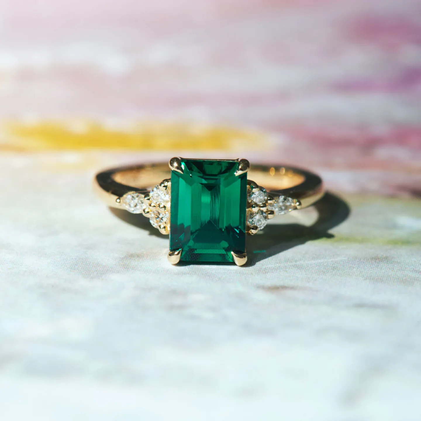 Emerald-cut green emerald engagement ring in yellow gold with round diamond sides