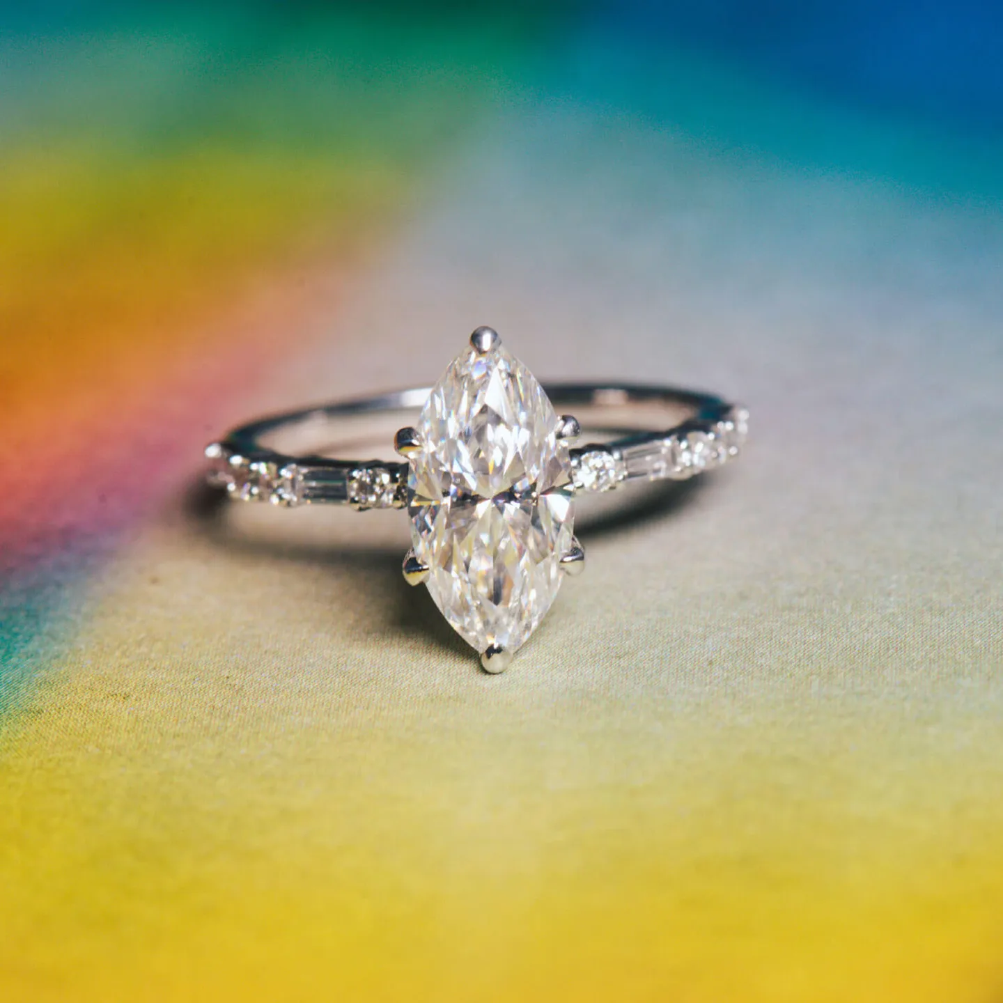 Marquise moissanite engagement ring in white gold with accent stones against a rainbow backdrop