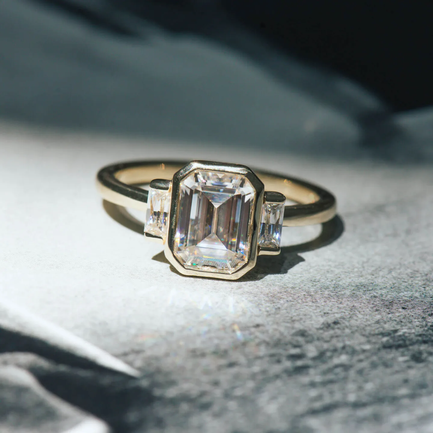 Emerald-cut moissanite three-stone engagement ring in yellow gold with baguette side stones