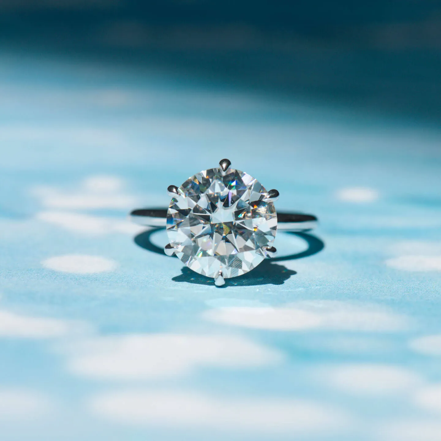 Round moissanite six-prong solitaire engagement ring in white gold on a blue backdrop