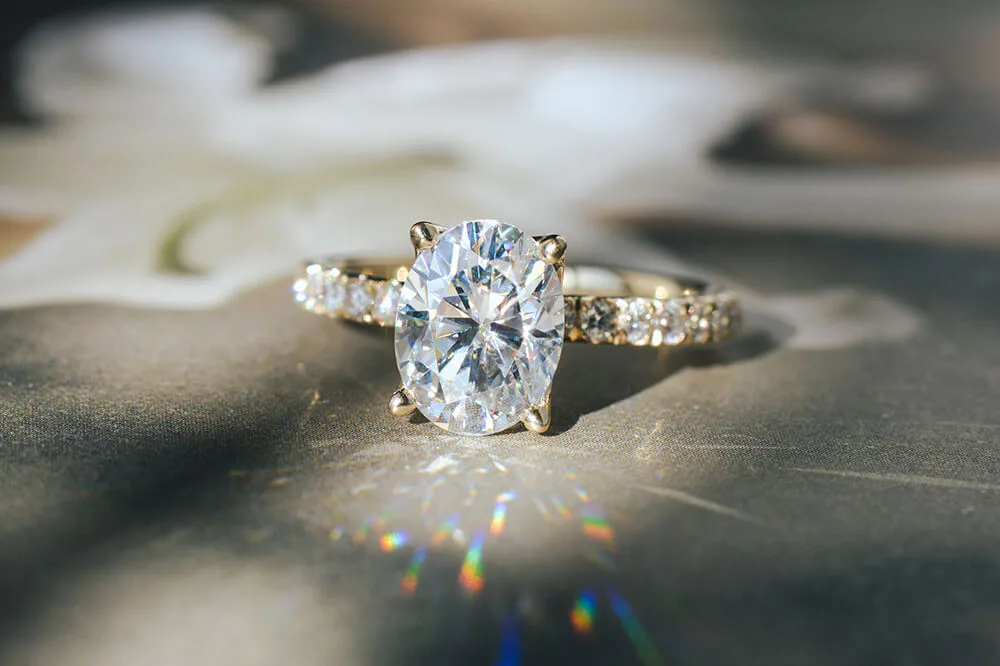 Oval moissanite engagement ring in yellow gold with a diamond-set band, throwing rainbow sparkle
