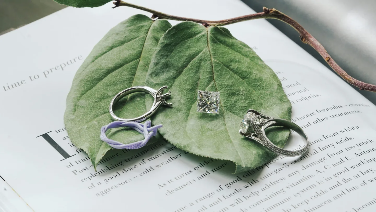 Engagement rings and a purple resin model of a ring resting on a green leaf over an open book