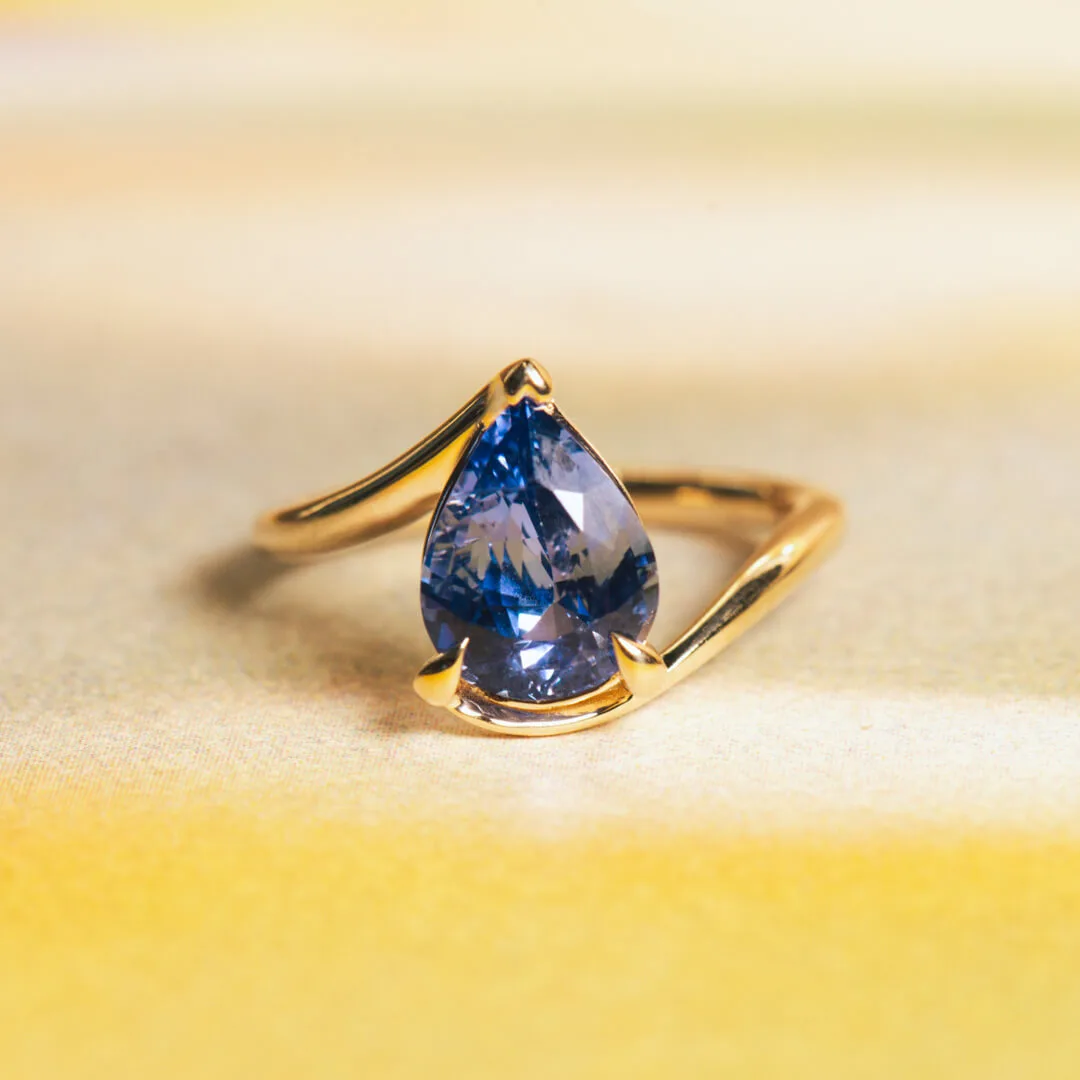 Pear-shape blue sapphire engagement ring in yellow gold with a diamond accent