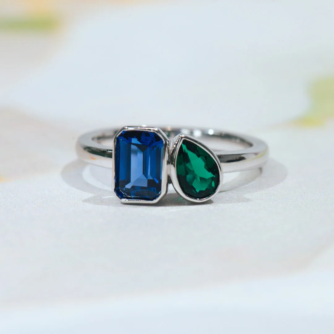 Toi et moi ring in white gold with a bezel-set blue sapphire and a pear-cut emerald