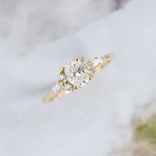 A 14k gold ring featuring an oval center stone with smaller round and pear side stones.